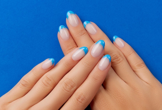 Beautiful womans hands trendy nail design on blue background Manicure pedicure beauty salon concept