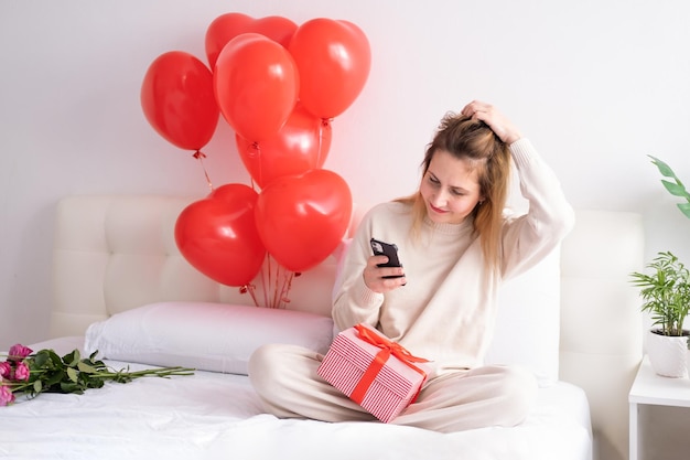 Beautiful women in casual cozy clothes using phone on bed celebrating valentine day