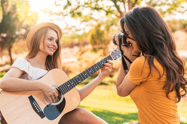Красивые женщины весело играют на гитаре и фотоаппарате в парке. Друзья и летняя концепция.