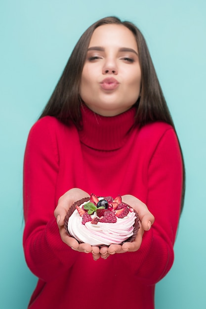 Beautiful women holding small cake. Birthday, holiday, diet. Studio portrait over blue background