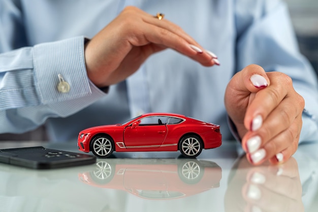 Beautiful women's hands at the table make conditional protection of a small machine concept of car insurance protect car drivers