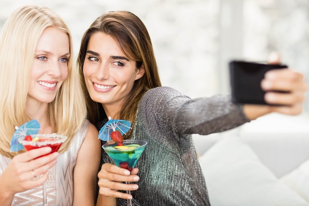 Belle donne che prendono selfie con il telefono cellulare e che hanno mocktail