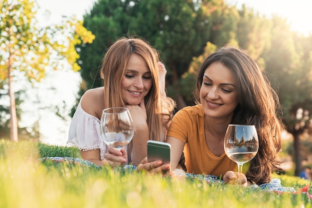 Beautiful women using mobile in the park. Friends and summer concept.