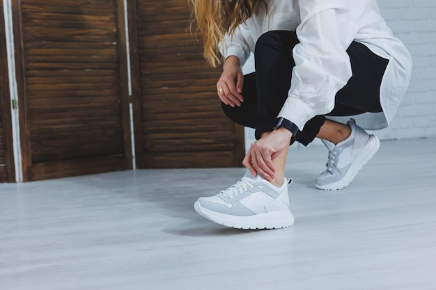 Beautiful womens shoes with legs leather white sneakers in the interior of a room or office shoes for a woman black trousers and white sneakers casual and modern style modern and trendy