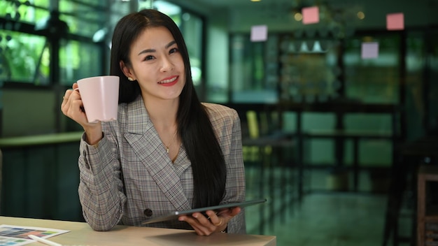 Bella donna lavoratrice che tiene tazza di caffè e sorride alla telecamera