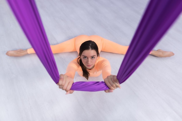 A beautiful yogi woman practices aerial yoga in a purple hammock in a fitness club View from above