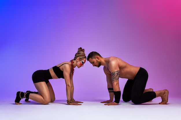 Beautiful young acrobats or gymnasts with colorful face painting on pink blue gradient background Professional ballet couple dancing Emotional duet performing choreographic art Animal instinct