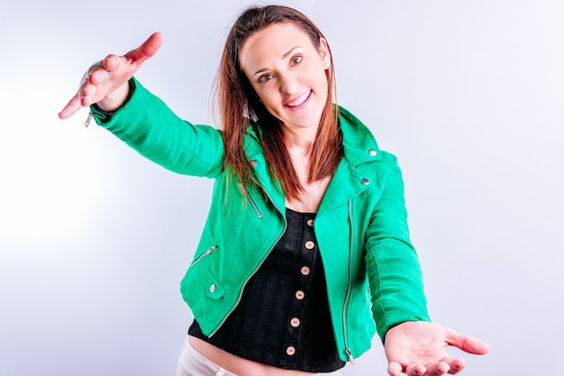 Beautiful young adult woman in green jacket showing offering a hug with raised arms with serious gesture with white background with copyspace.