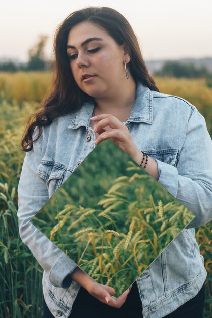 Beautiful young adult woman with a mirror in her hands in a rye field