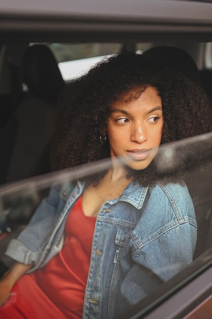 Bella giovane donna afroamericana autista dai capelli neri in giacca di jeans seduto in una nuova auto marrone