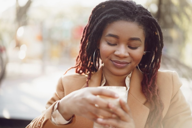 屋外カフェに座って、コーヒーを飲む美しい若いアフリカ系アメリカ人女性