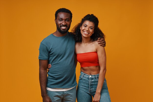 beautiful young african couple looking at camera and smiling while standing against yellow background
