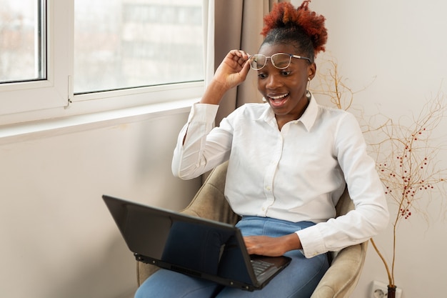 beautiful young african female sitting with a laptop indoors near the window with a surprised face