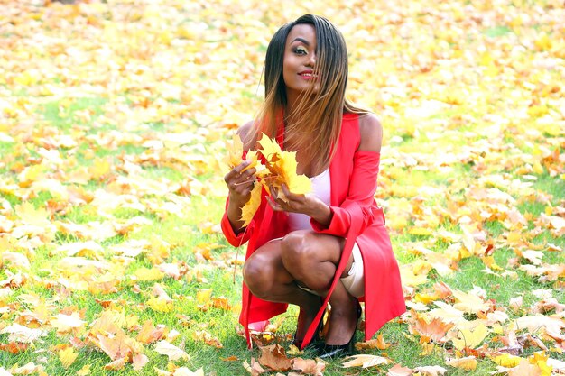 Beautiful young African girl collects autumn leaves in the Park