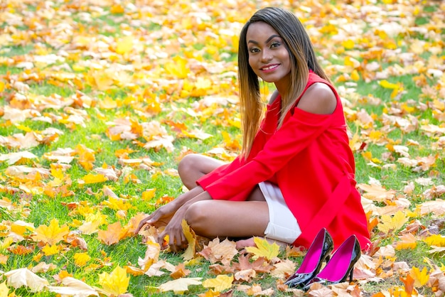 La bella ragazza africana raccoglie le foglie di autunno nel parco