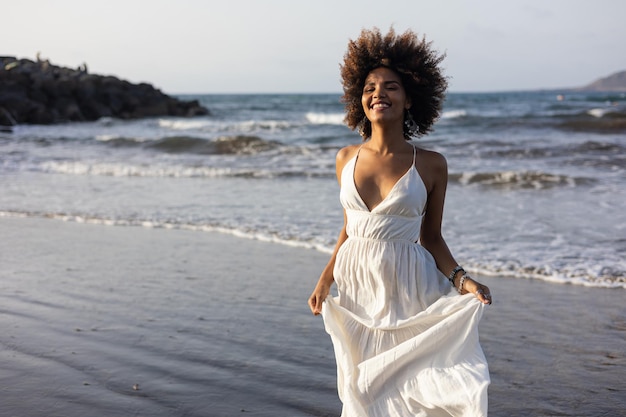 해변을 따라 행복하게 달리는 하얀 드레스를 입은 아름다운 아프리카 소녀