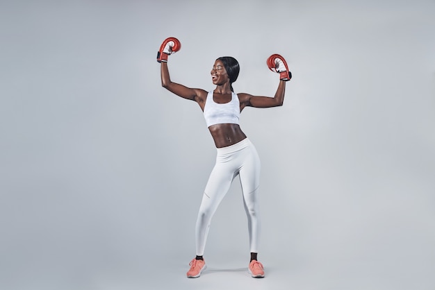 Bella giovane donna africana in guantoni da boxe che tiene le braccia alzate