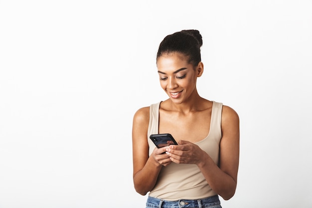 Beautiful young african woman casually dressed standing isolated, using mobile phone