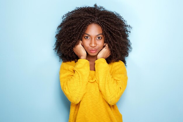 Beautiful young african woman holding ears on blue background