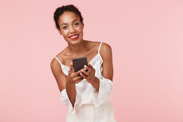 Beautiful young african woman isolated over pink backgroung wall using mobile phone