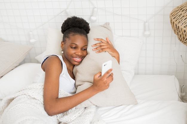 beautiful young african woman lies on a white bed with a phone