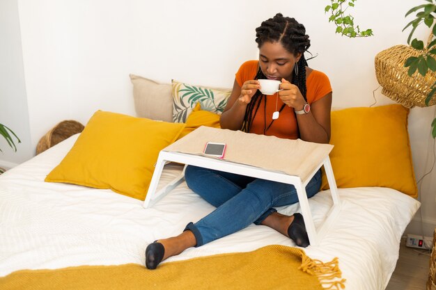 beautiful young african woman sitting in bed drinking tea