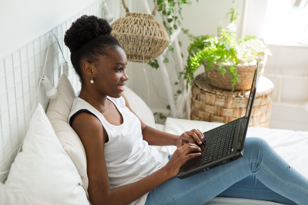 beautiful young african woman sitting on bed with laptop