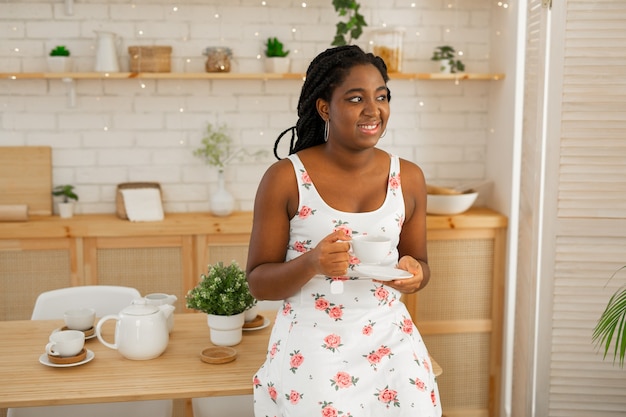 お茶を飲む台所で夏のドレスを着た美しい若いアフリカの女性
