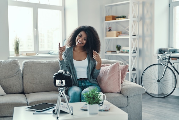 Beautiful young African woman telling something and smiling while making social media video