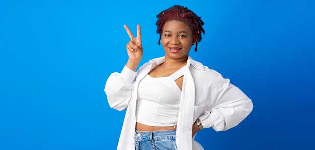 Beautiful young afro woman showing victory sign against blue background