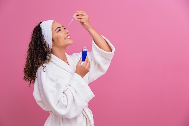 Beautiful young afro woman with cosmetic oil on color background