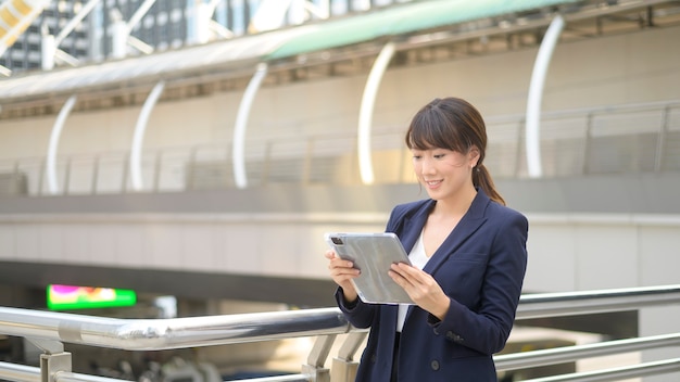 Beautiful young asian business woman is using tablet in modern city