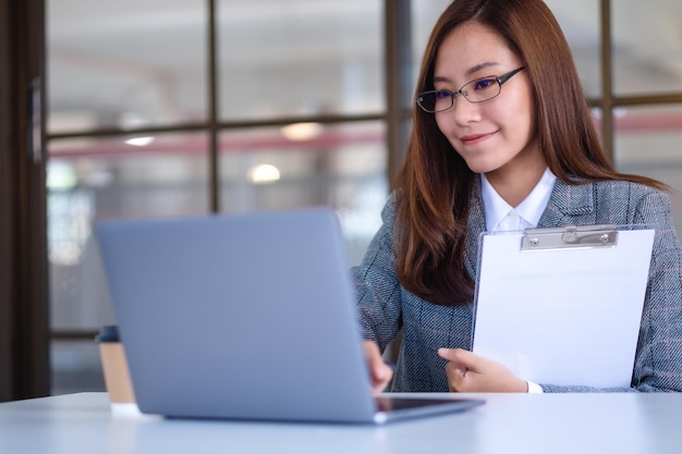 사무실에서 일하는 동안 노트북 컴퓨터를 사용하는 아름다운 젊은 아시아 여성