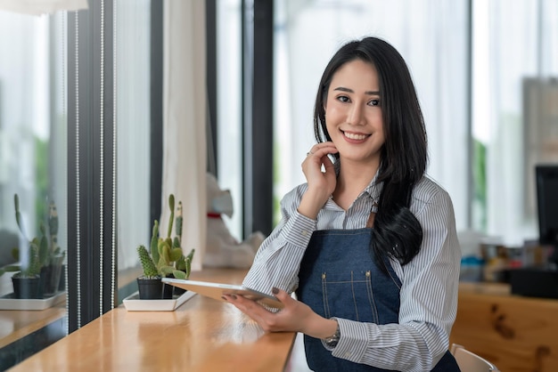 Beautiful young Asian businesswoman owner holding a tablet at a cafÃ©. Looking at the camera.