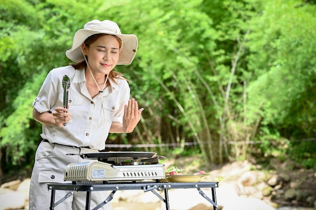 Beautiful young Asian female cooking her picnic lunch smelling steam of a delicious steak