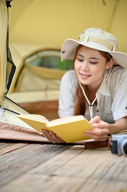 美しい若いアジアの女性は、彼女のテントで身も凍るように横たわっている間、本を読んでリラックスします