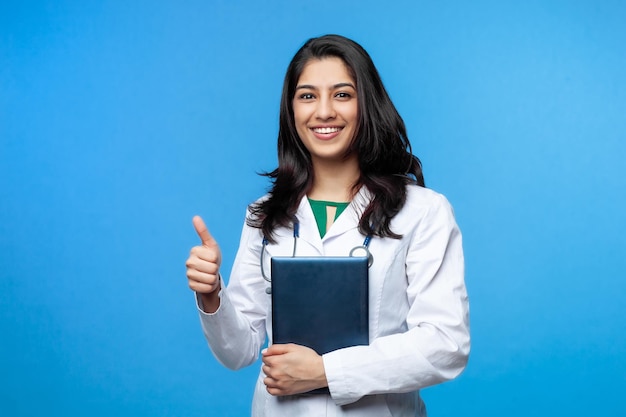 Beautiful young Asian girl doctor, with a laptop for records isolated on a blue background. Medical student general practitioner. The concept of medical education in India