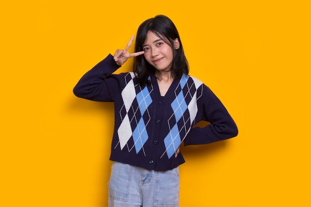 Beautiful young asian girl showing peace or victory hand gesture on yellow background