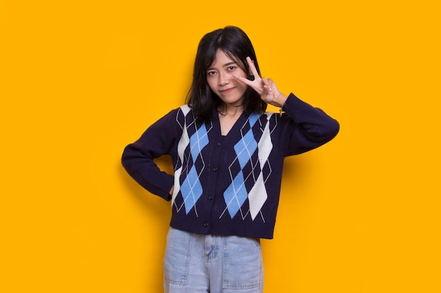 beautiful young asian girl showing peace or victory hand gesture on yellow background