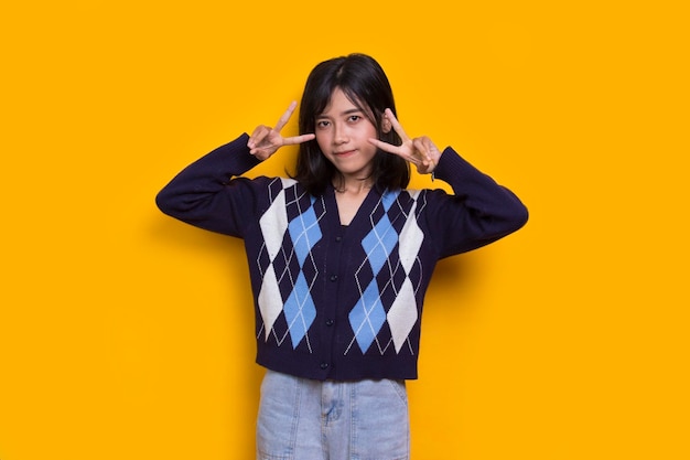 beautiful young asian girl showing peace or victory hand gesture on yellow background