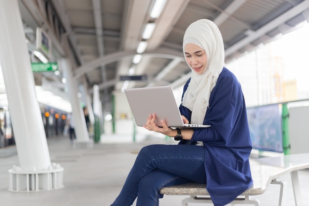 Beautiful young Asian girl working at a skytrain with a laptop. Muslim women