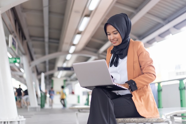 Beautiful young Asian girl working at a skytrain with a laptop. Muslim women