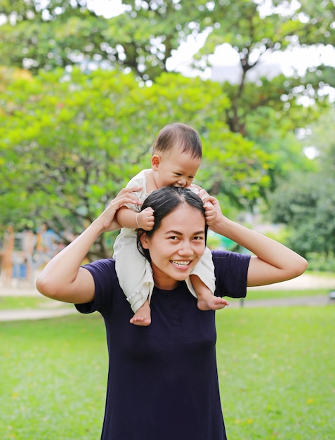 自然公園でママの肩に乗って幸せな男の子と美しい若いアジアの母親。