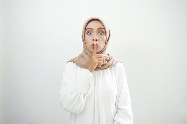 Beautiful young asian muslim woman wearing casual clothes asking to be quiet with finger