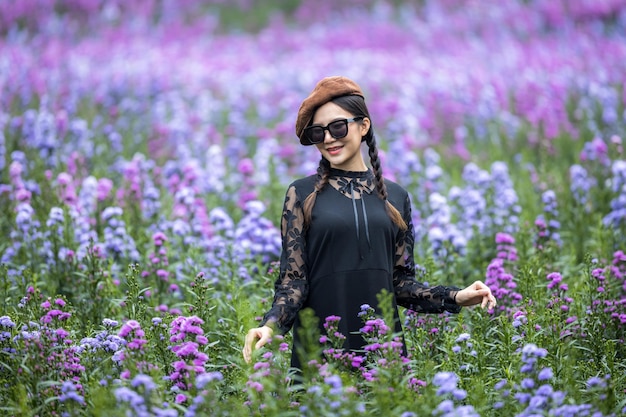 Beautiful young asian woman on black dress with black sunglasses on violet flower field., Aroma concept,  Attractive young asian female outdoors touching violet flowers.