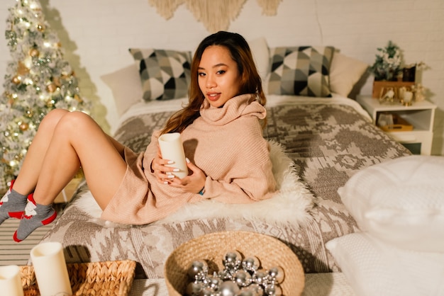 Beautiful young asian woman celebrating christmas at home, having fun while opening presents