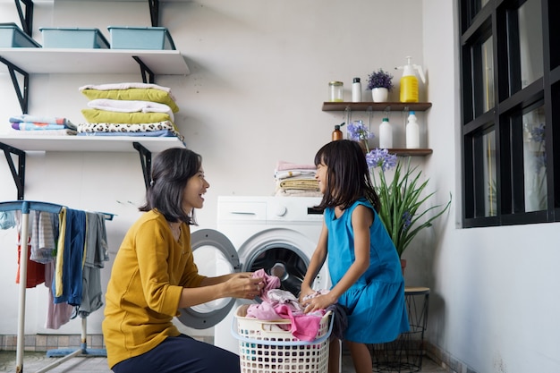 美しい若いアジアの女性と子供の女の子の小さなヘルパーは家で洗濯をしています。
