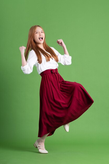 Beautiful young Asian woman dancing and posing on green background