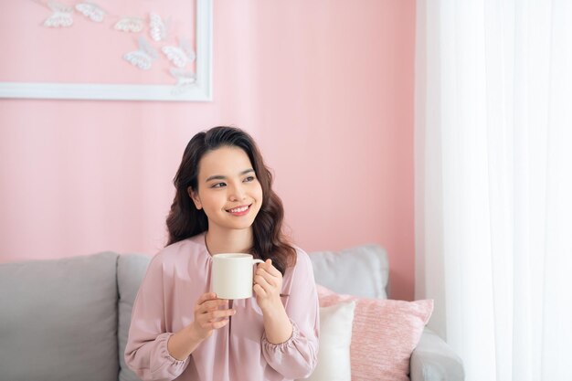 コーヒーを飲みながらソファでくつろぐ美しい若いアジア人女性
