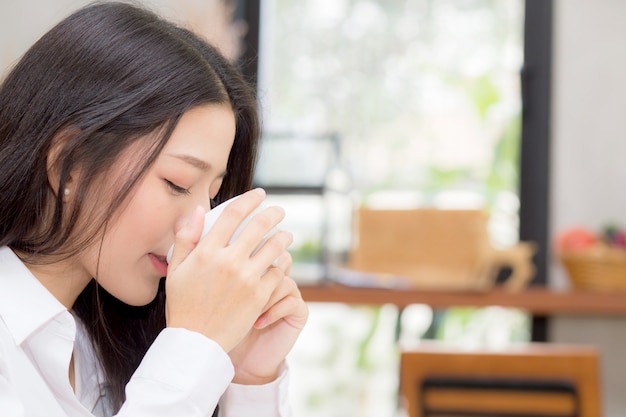 美しい若いアジアの女性はコーヒーを飲んで、朝はカフェで笑顔。